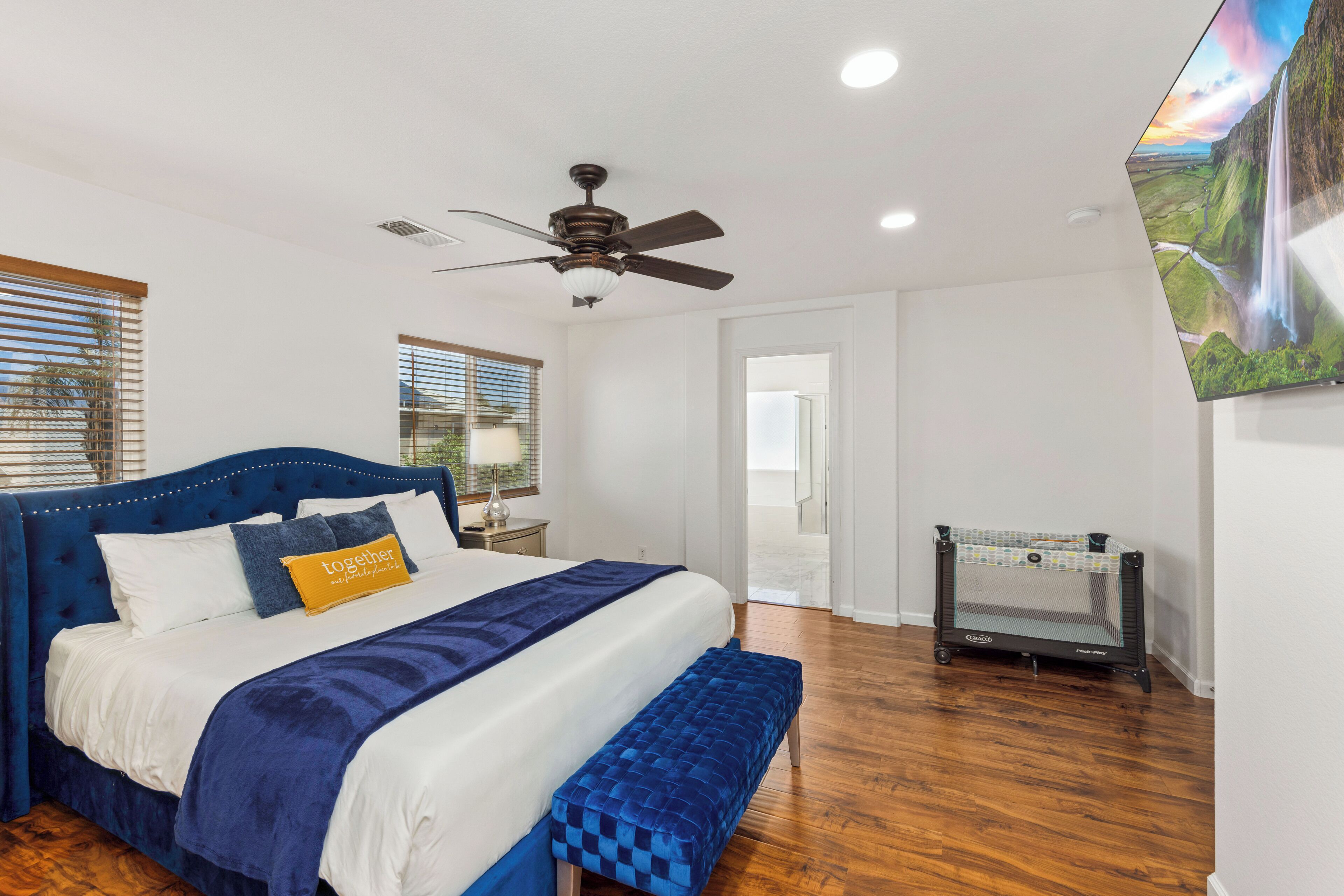 A bedroom with a bed, a ceiling fan, a TV, and a crib.