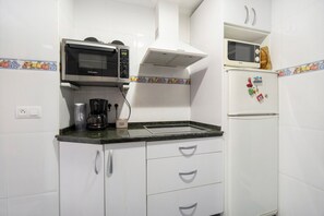 Una cocina con armarios blancos, microondas, cafetera y refrigerador.