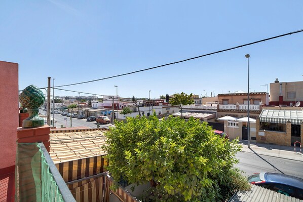 Zona residencial con vista a la calle, un árbol verde grande y un edificio con techo de tejas.