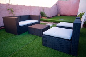 Un patio con mobiliario de mimbre y césped artificial.