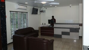 Um saguão de hotel moderno com um balcão de recepção, um sofá de couro marrom e uma grande janela com grades de metal.