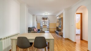 A modern living room with a dining table, two chairs, a sofa, and a TV.