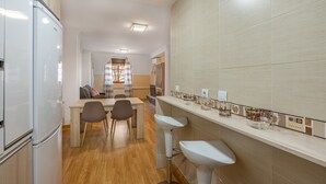 A modern kitchen with a refrigerator, two bar stools, a dining table with chairs, and a tiled backsplash.
