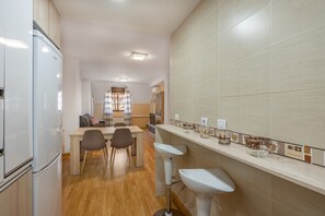 A modern kitchen with a refrigerator, two bar stools, a dining table with chairs, and a tiled backsplash. - Apartment "Ladera de Sierra Nevada" with Mountain View & Wi-Fi (Monachil)