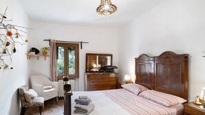 A bedroom with a bed, a chair, a dresser, a mirror, and a window.
