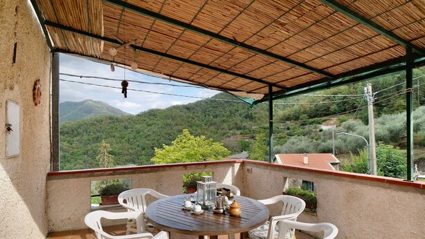 A covered outdoor seating area with a table and chairs, overlooking a mountainous landscape.