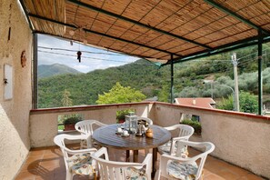 A covered outdoor seating area with a table and chairs, overlooking a mountainous landscape.