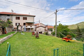 A residential area with a house, a grassy yard, a wooden chair, and a red and yellow object.
