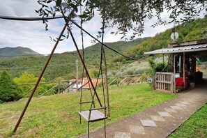 A rural setting with a swing set, a wooden structure with a satellite dish, and a path leading to a house.