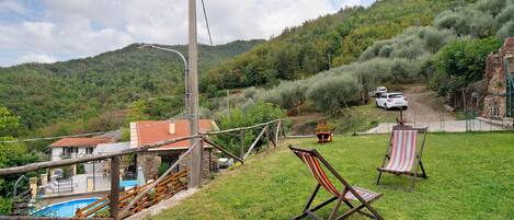 Ein Anwesen an einem Hang mit Swimmingpool, Holzterrasse und zwei Liegestühlen.