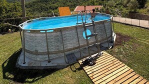 An outdoor swimming pool with a wooden deck, surrounded by a grassy yard and a mountain backdrop.