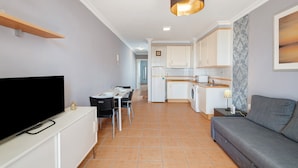 Un espace de vie compact comprenant un téléviseur à écran plat, un canapé, un coin repas et une kitchenette.