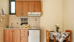 A compact kitchen with wooden cabinets, a white refrigerator, and a dining table with a patterned tablecloth. - Studio "Daratos 4" with Shared Garden & Wi-Fi (KEFALONIA)