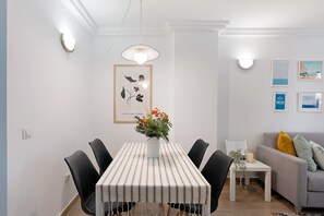 A dining area with a striped tablecloth, black chairs, a vase of flowers, and wall-mounted light fixtures.