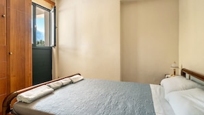 Un dormitorio con cama, un armario de madera, una mesita de noche con lámpara y ventana con vistas.