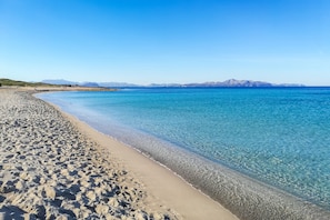A beach with clear blue water, a sandy shore, and distant mountains. - Villa 'Bohemi' Seafront, Wi-Fi and A/C in Bedrooms (Son serra de Marina)