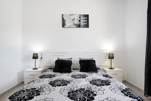 A bedroom with a bed, two nightstands, two black fluffy pillows, a wall-mounted artwork, and a black curtain.