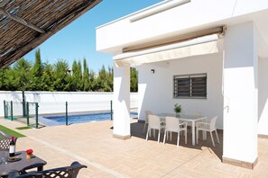 A covered patio with a pool, outdoor seating, and a white building.