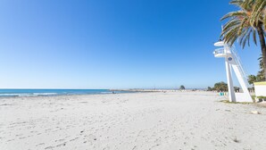 Una playa con un faro blanco, palmeras y un cielo azul despejado.