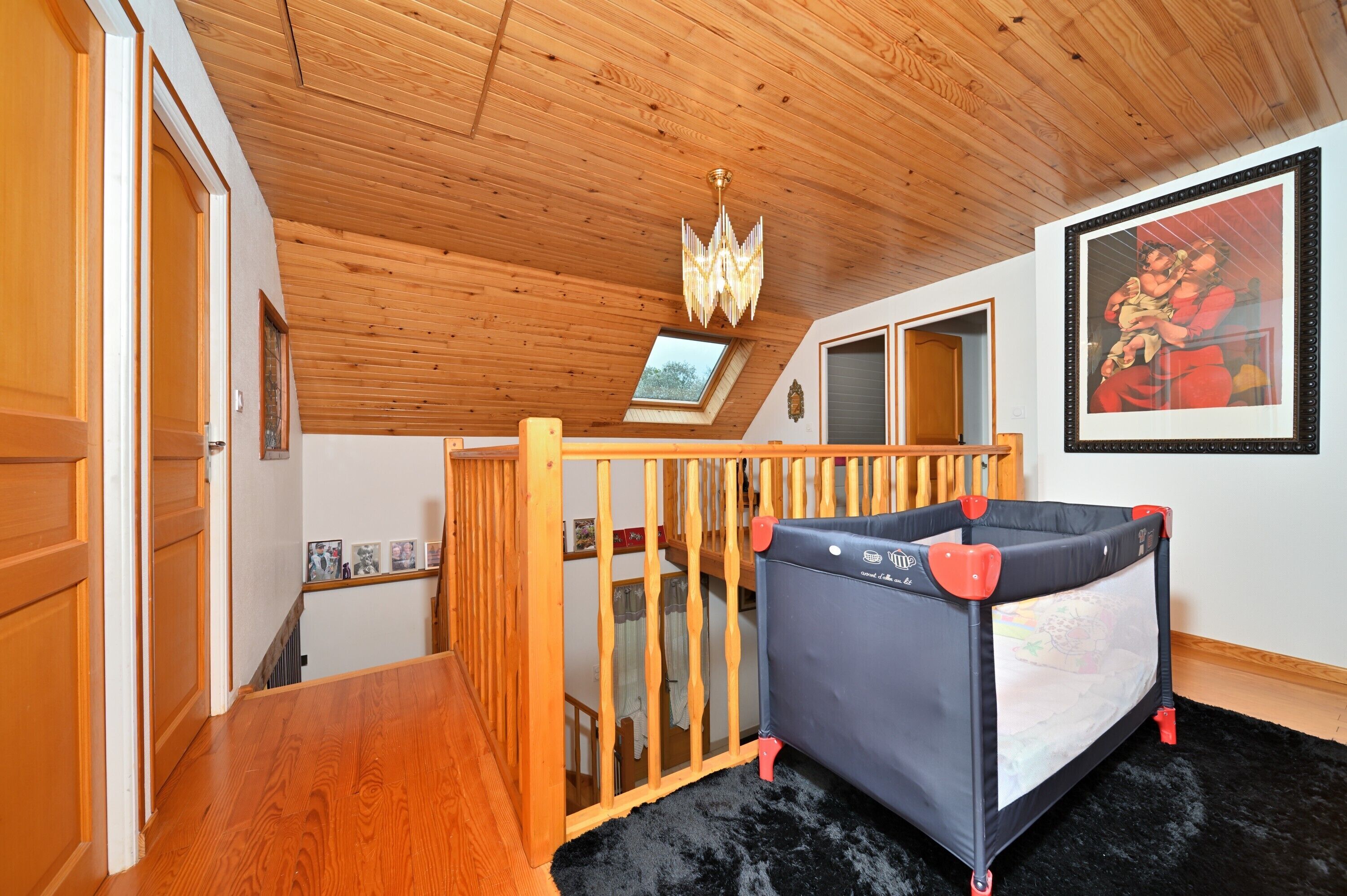 Une pièce avec un plafond en bois, un berceau, un tapis noir et un tableau encadré accroché au mur.