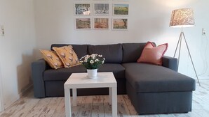 A living room with a dark grey sofa, a white coffee table, and a floor lamp. There are six framed pictures on the wall above the sofa. - Lake House Lebehn (Lebehn)