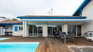 Een zwembadgedeelte met een houten terras, een whirlpool en buitenmeubels.