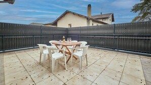 Eine Terrasse mit rundem Tisch und Stühlen, einem Zaun und einem Gebäude im Hintergrund.