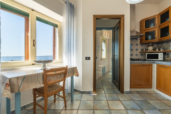 A kitchen with a dining table and chairs, a view through an open door, and wooden cabinets. - Holiday Home "Cà du Savio" with Sea View and Wi-Fi (Calasetta)