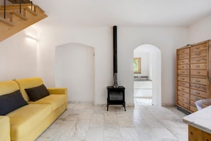 A living room with a yellow sofa, a black fireplace, a wooden cabinet, and a marble floor.