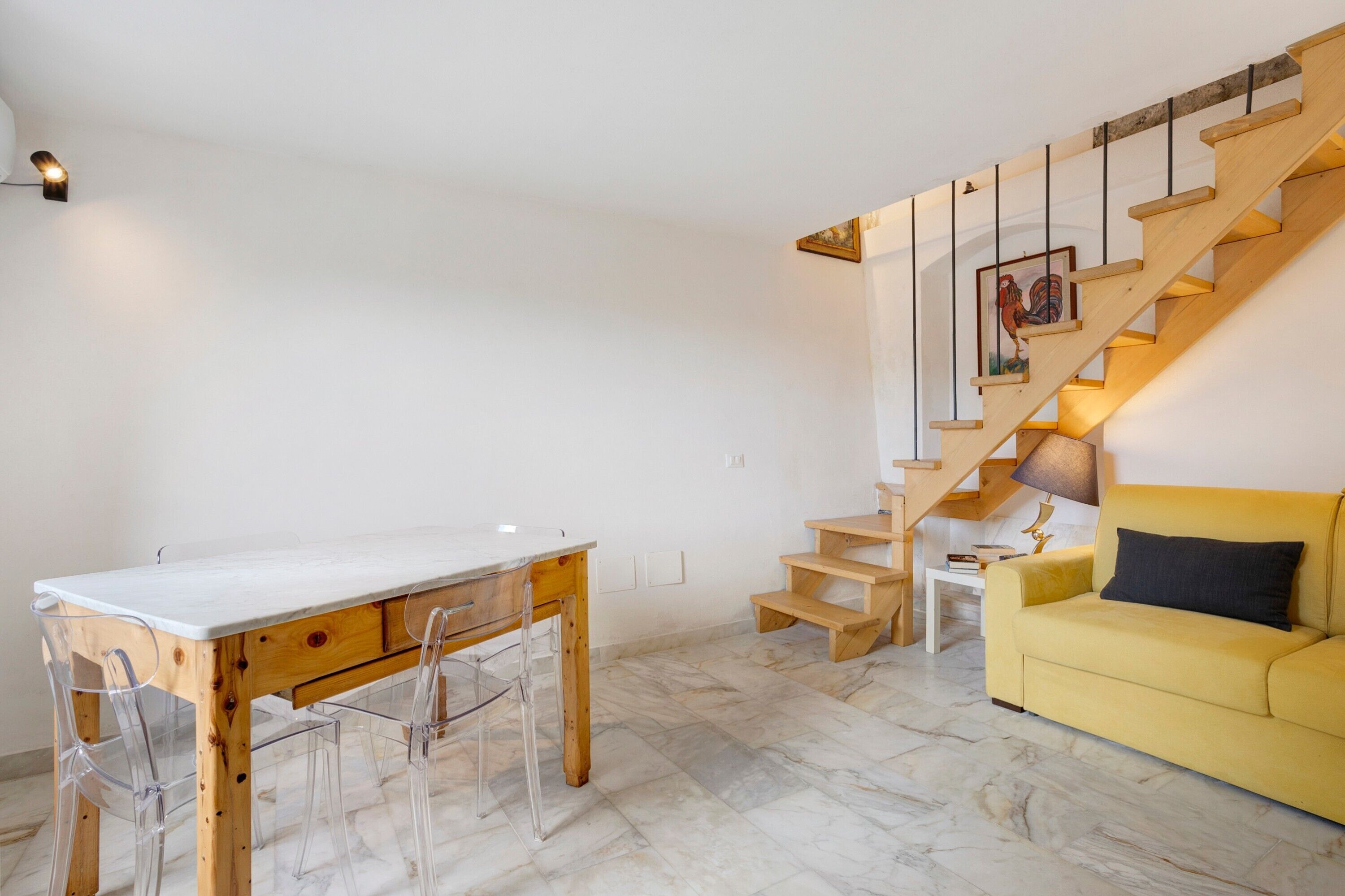 Un espace de vie moderne avec un escalier en bois, une table à manger avec des chaises et un canapé jaune.