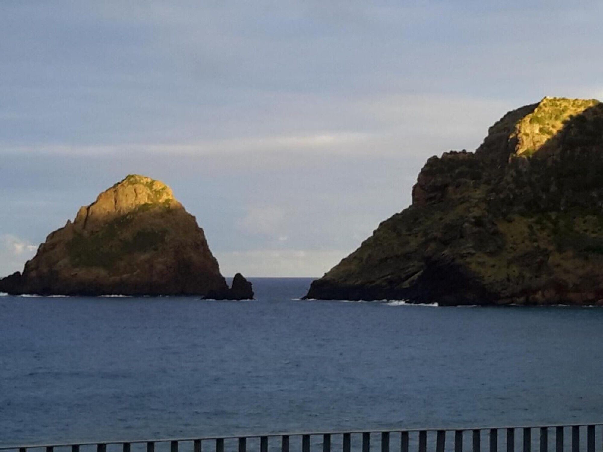 A coastal landscape with two prominent rock formations and calm sea.