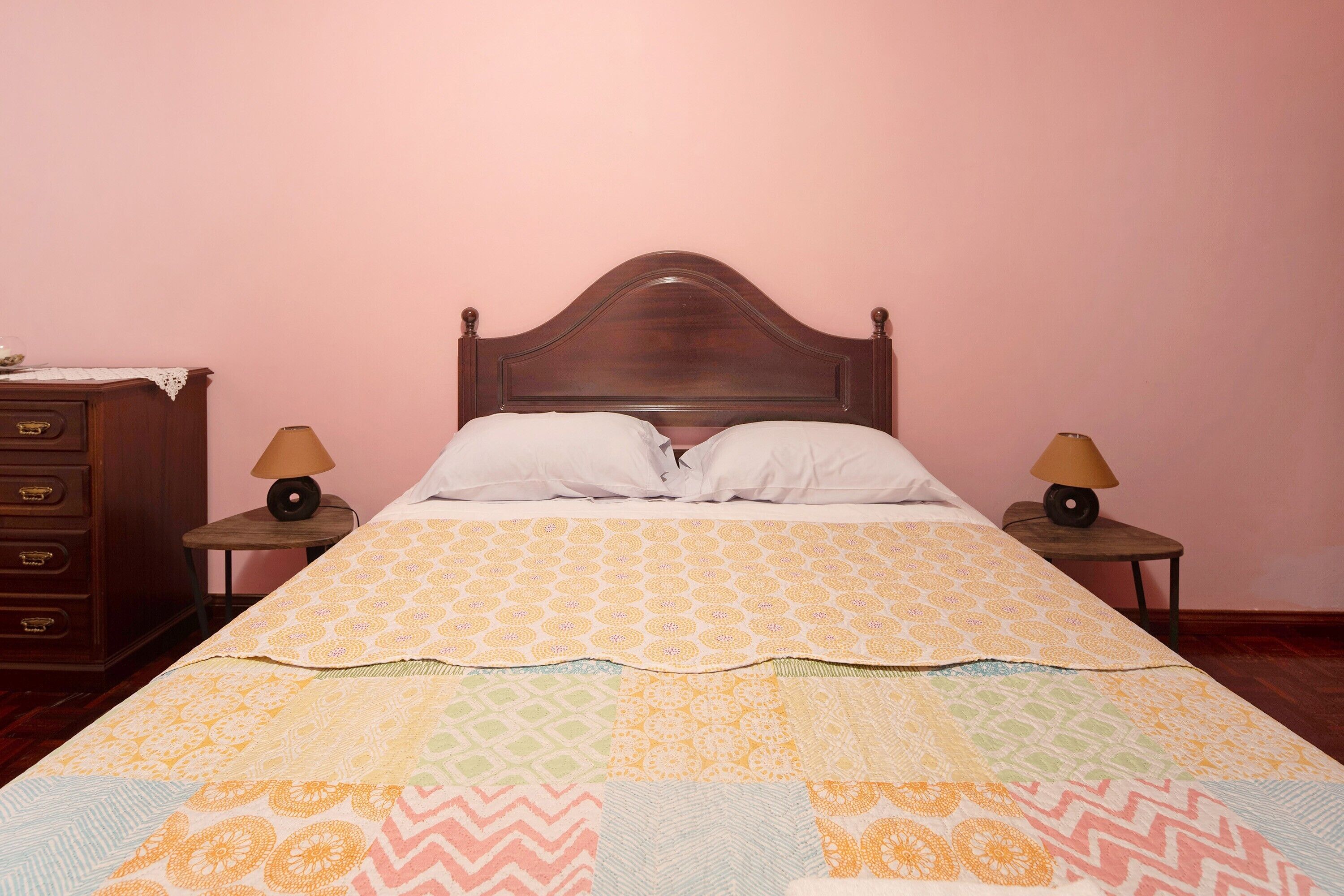 A bed with a patterned bedspread, two bedside lamps, a wooden headboard, and a nightstand with a lamp.
