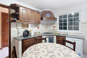 Una cocina con armarios de madera, estufa a gas, lavavajillas y una ventana con persianas.