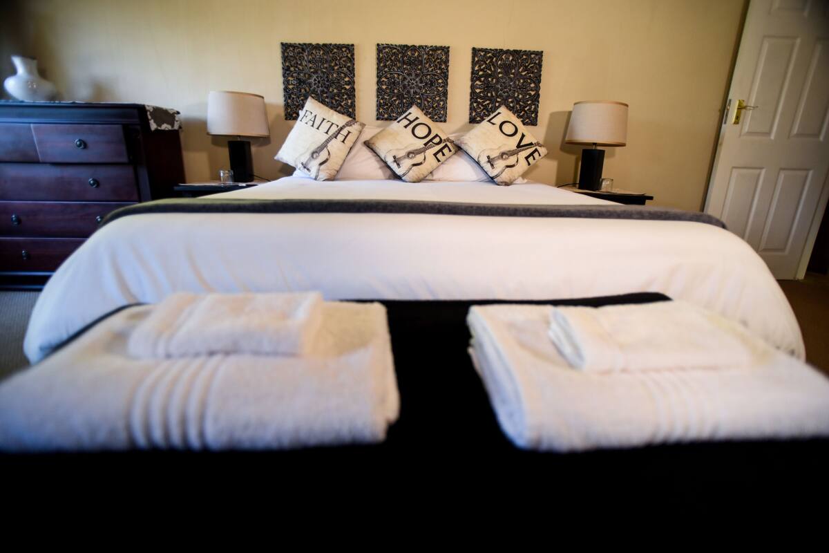A neatly made bed with three decorative pillows, a dresser, and two bedside lamps.