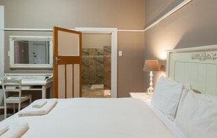Habitación de hotel con cama, escritorio con silla, espejo, baño con ducha y lámpara de noche.