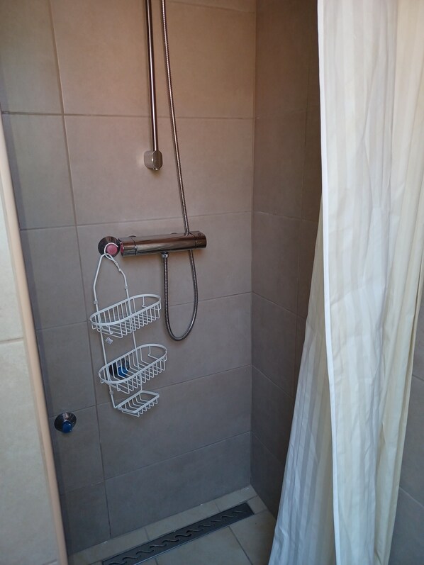 A shower with a metal hose and a white shower caddy.