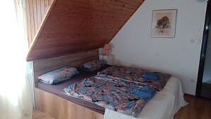 Una camera da letto con soffitto spiovente, pareti in legno, un letto con lenzuola a fiori, un comodino e una lampada fissata alla parete.