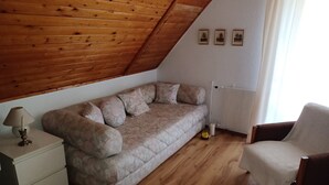 Una stanza accogliente con soffitto in legno, un divano con cuscini, un tavolino con lampada, una poltrona e un termosifone.