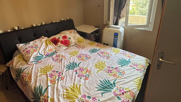 A bedroom with a bed, a window with curtains, a ceiling light fixture, and a wall-mounted air conditioner. - Appartement T4 à 5 min du Stade Vélodrome (Marseille)