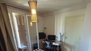 A bedroom with a checkered bedspread, a desk with a computer, and a standing lamp. - Appartement T4 à 5 min du Stade Vélodrome (Marseille)