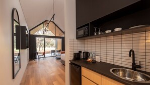 A modern kitchen with a black countertop, stainless steel sink, and a microwave. There is a dining area with a table and chairs visible through large windows. - Par Five Shacks (Berri)