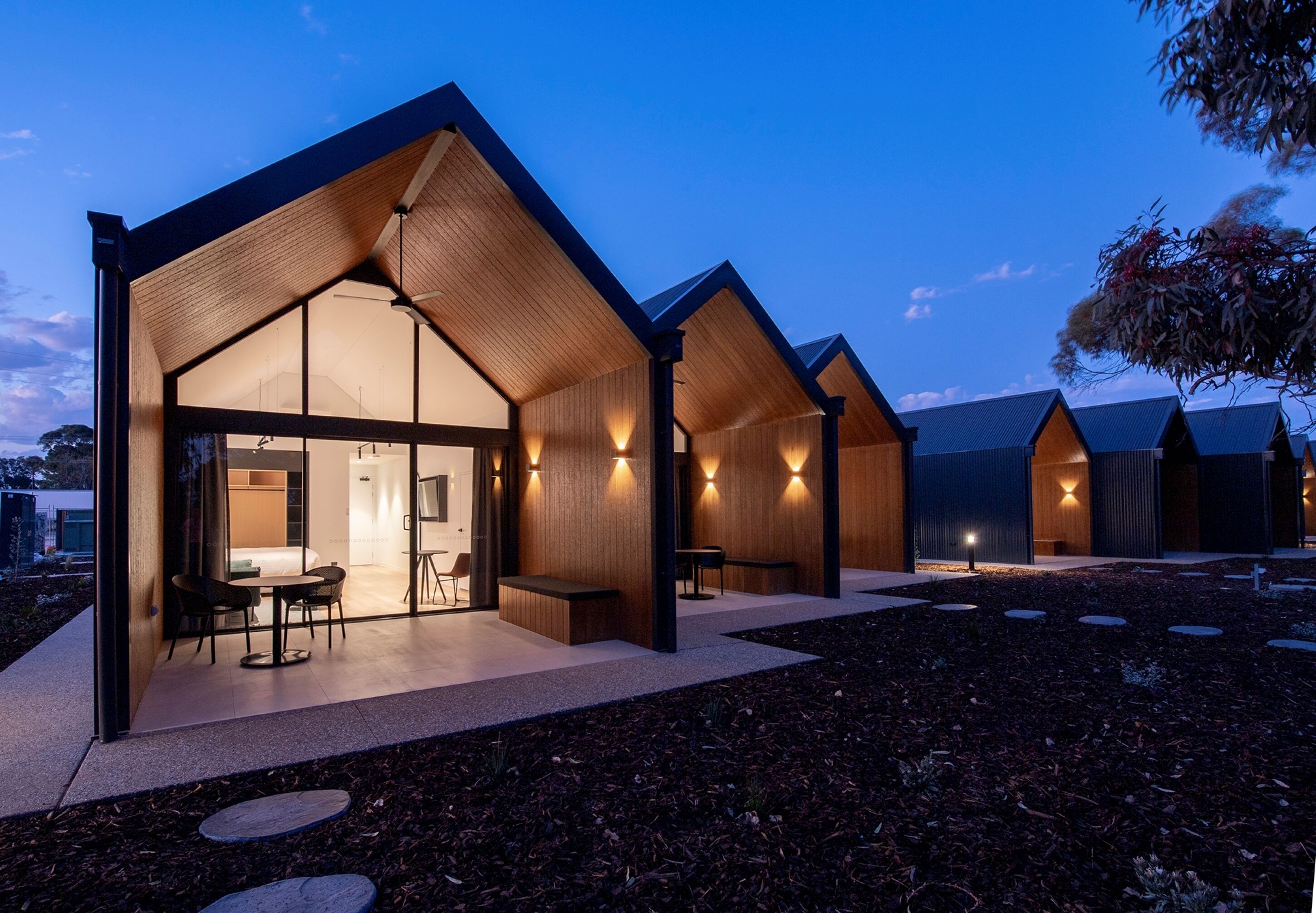 Un edificio moderno con una amplia entrada de vidrio, paredes interiores de madera y un patio con mobiliario.