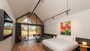 A modern bedroom with a large bed, a painting of flowers, and a view of the outdoors. - Par Five Shacks (Berri)
