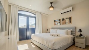 A modern bedroom with a large bed, a bedside table, an air conditioning unit, and a view through a door.