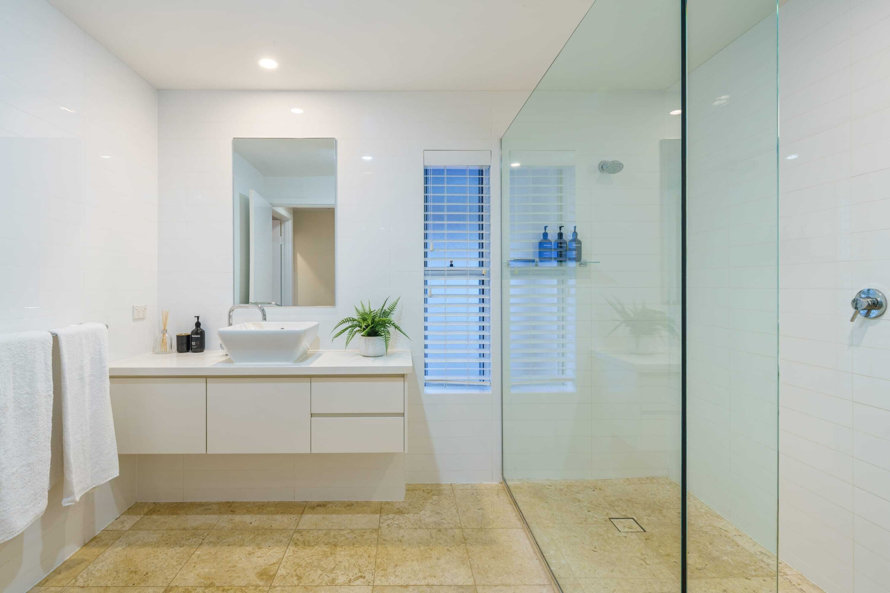 Un baño moderno con cabina de ducha de vidrio, un lavamanos blanco y un espejo encima.
