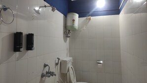 A bathroom with white tiles, a toilet, a shower, and a hand dryer. - Eight Lucky Homestay (West Kameng)