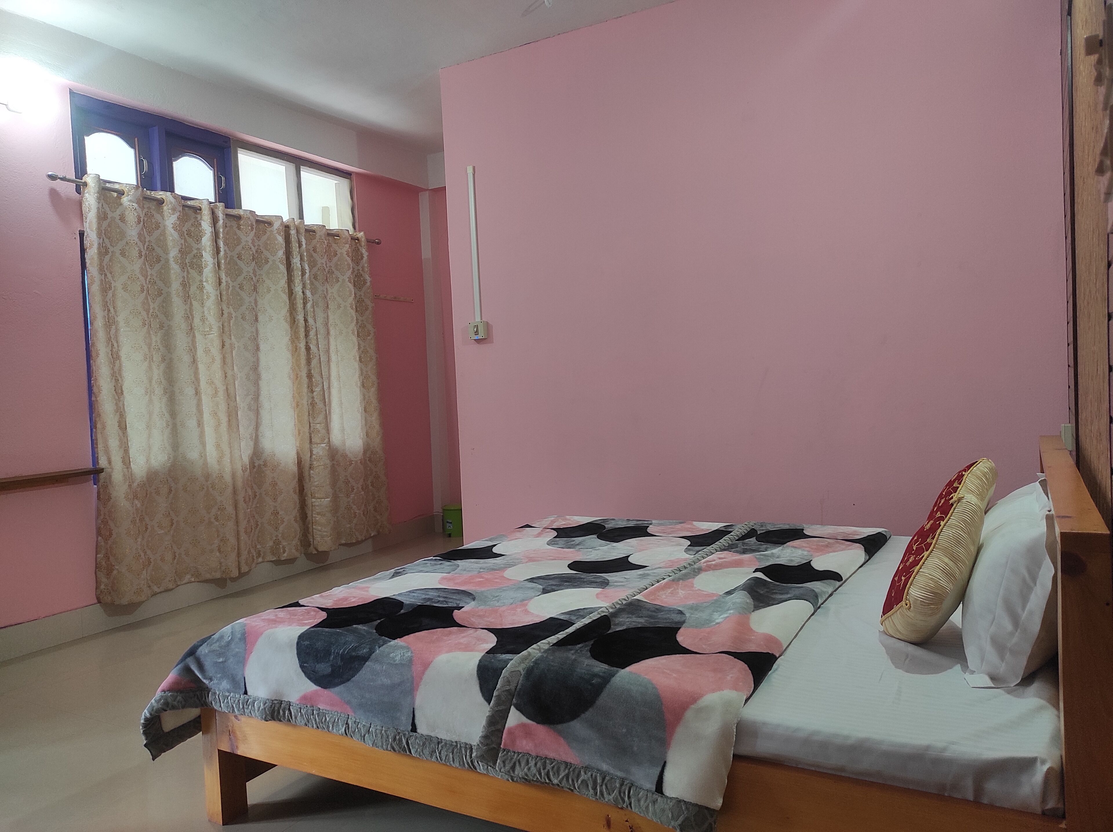 A bedroom with a bed, a window with curtains, and a pink wall.