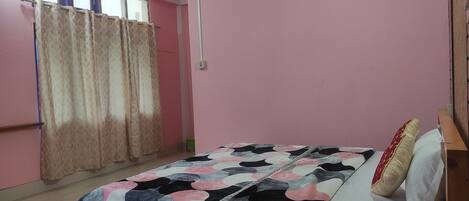 A bedroom with a bed, a window with curtains, and a pink wall.