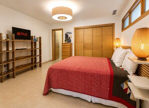 Un dormitorio con cama, televisión, estanterías de madera, armario y lámpara.