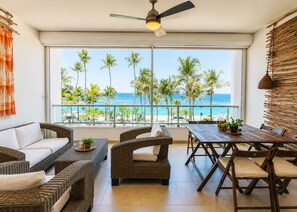 Un balcón con mobiliario de mimbre, una mesa con plantas y vista a la playa y al océano.